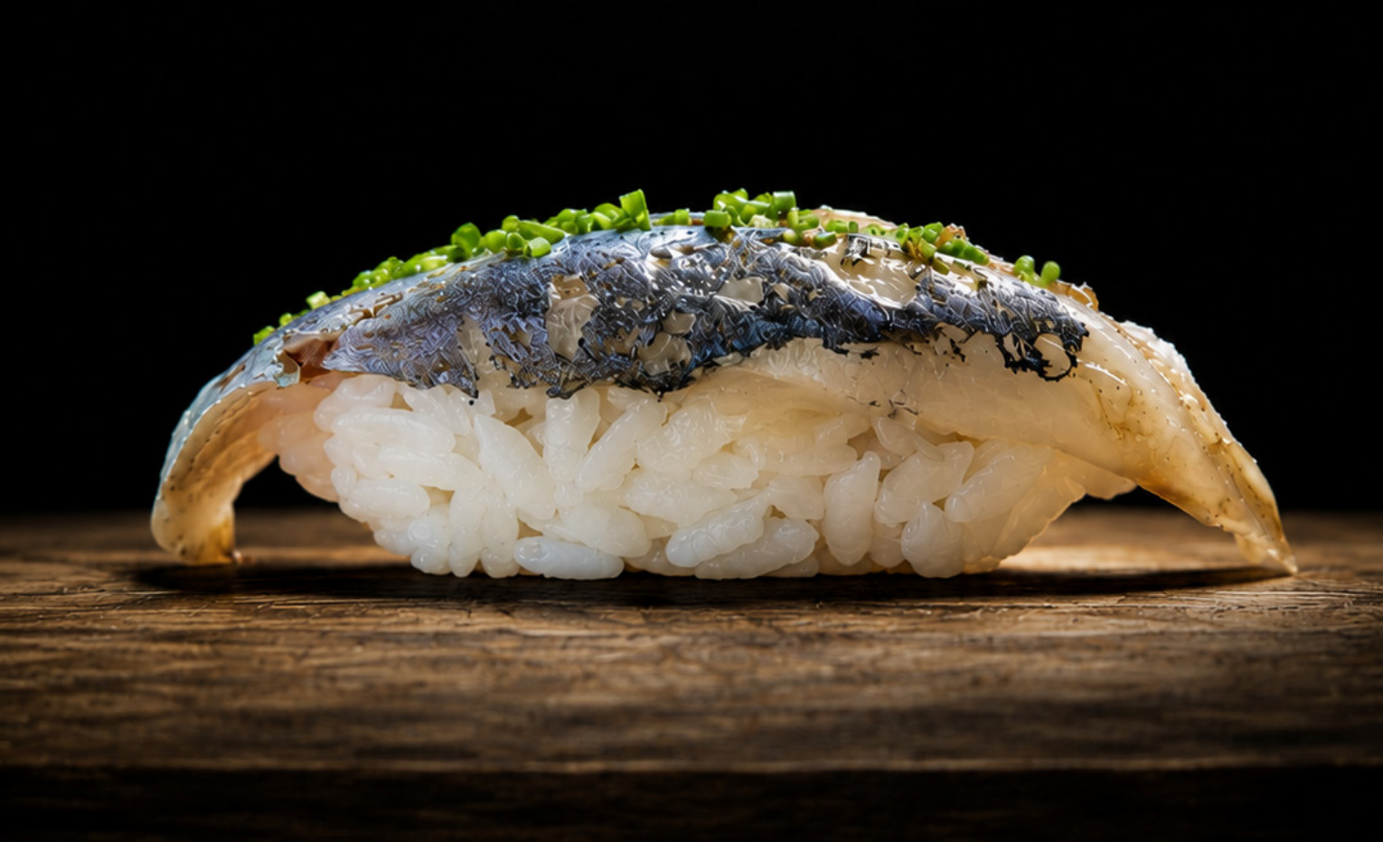 A complete piece of nigiri, presented on a wooden board against a dark background